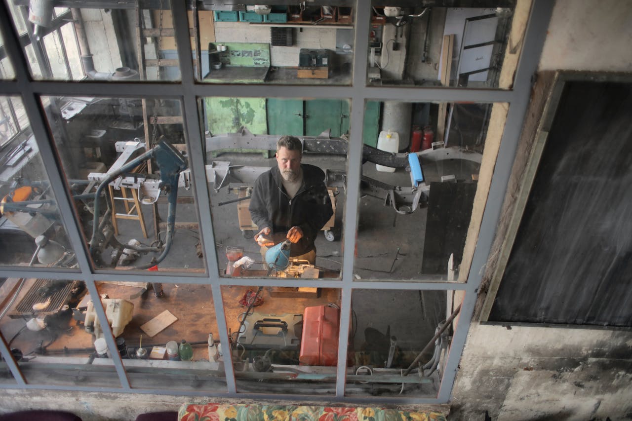 team-01 A man focuses on his work in a cluttered industrial workshop, viewed through a window.