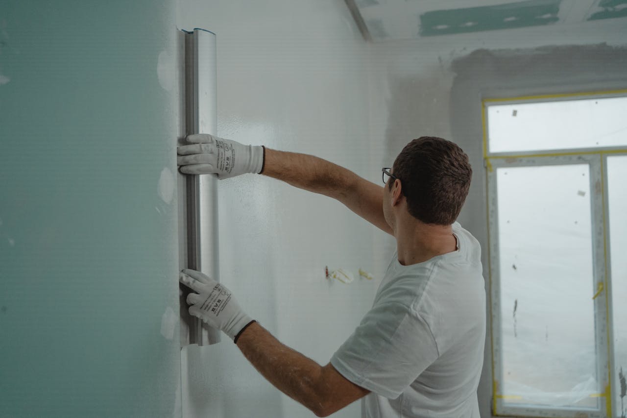 team-02 A man in a white shirt and gloves using a metal ruler for indoor wall renovation work.