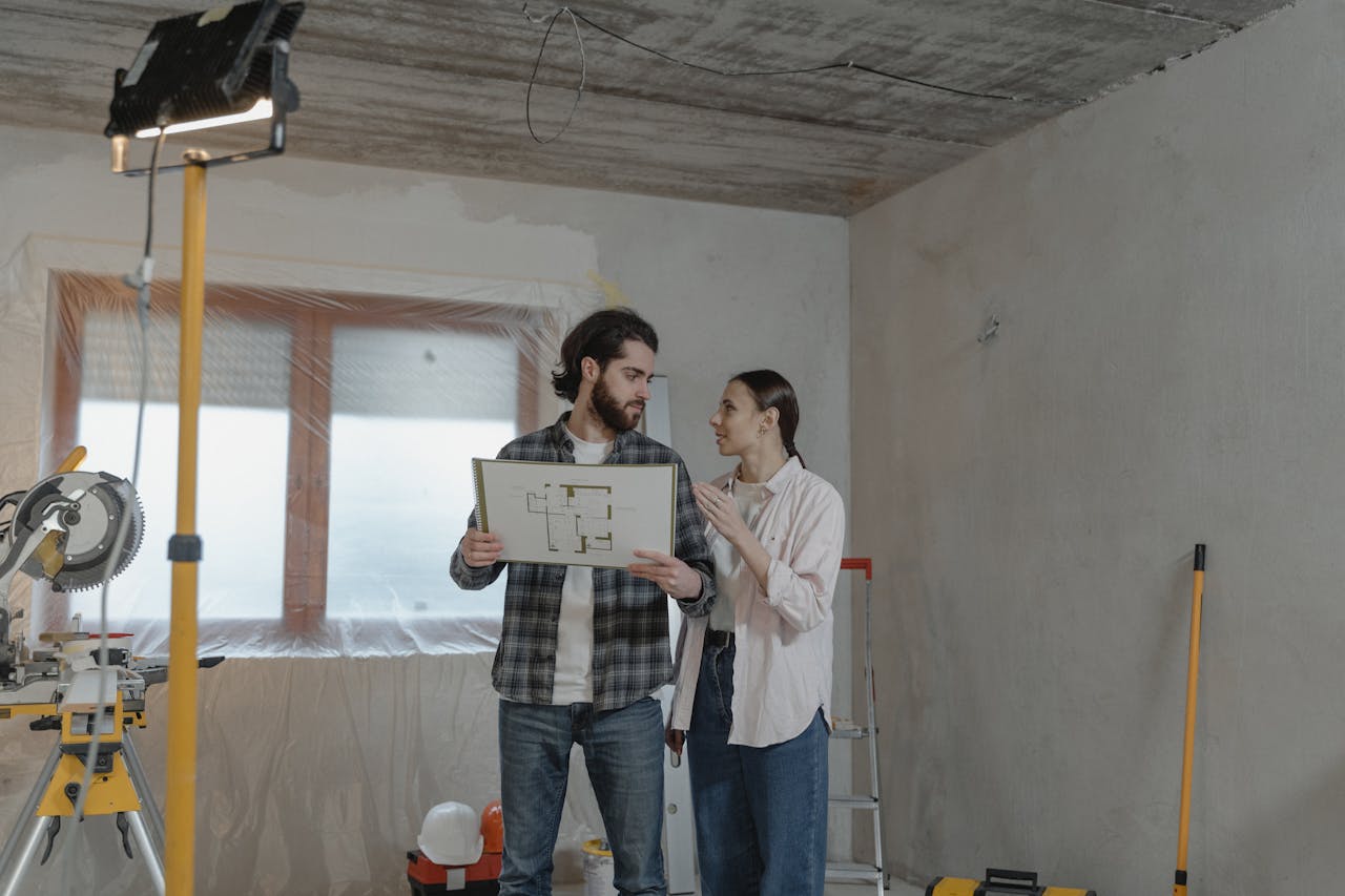 who-we-are A couple reviews a blueprint in a partially renovated room, planning home improvements.